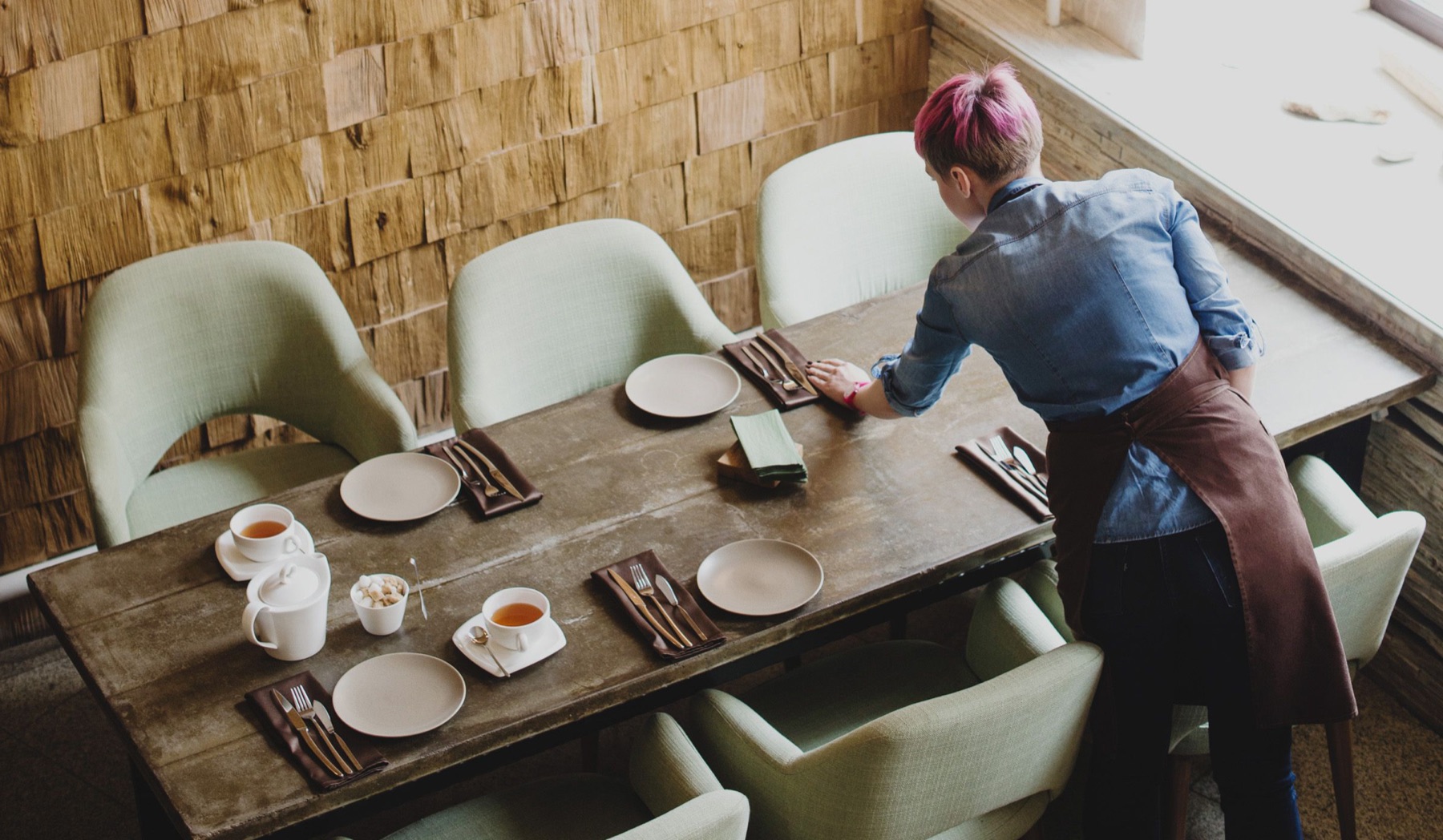 A server setting the table with tea service in a warm, busy dining room.